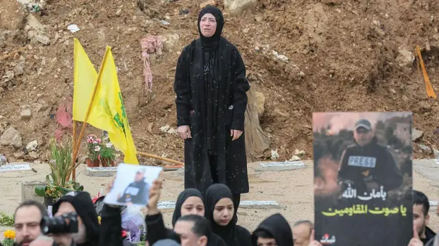 cenazeye katılan bir kalabalık, ellerinde öldürülen gazetecinin fotoğrafını tutuyorlar, arkada siyahlar giyinmiş çok üzgün bir kadın.