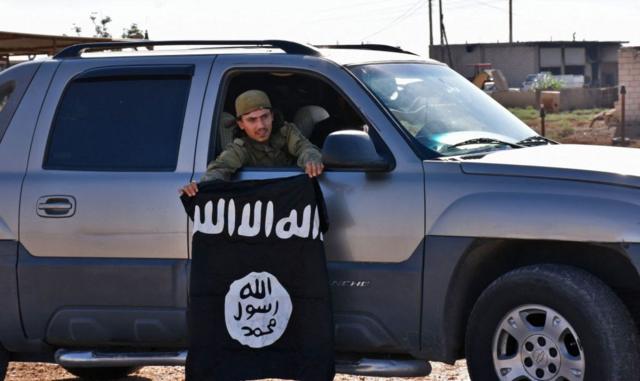 Um homem num carro exibe uma bandeira do Estado Islâmico