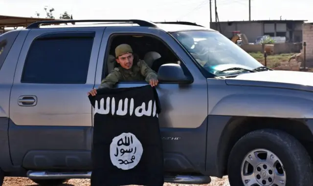 Um homem num carro exibe uma bandeira do Estado Islâmico