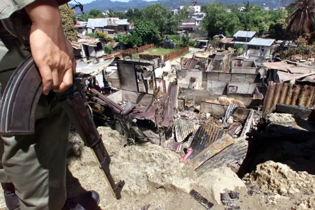 Seorang petugas bersenjata melihat bangunan yang terbakar setelah kerusuhan pecah di Ambon pada 1999.