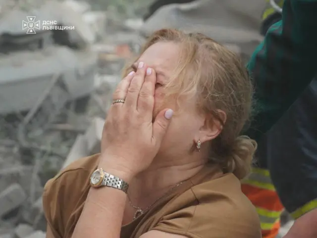 Жінка біля пошкодженого будинку у Львові, де рятувальники розбирають завали