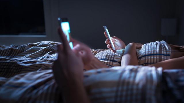 Deux personnes allongées dans un lit utilisant des téléphones portables