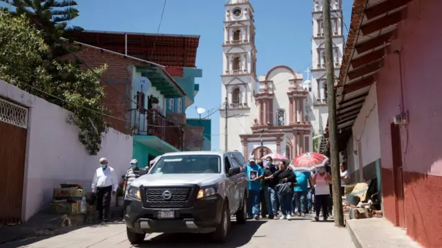 Con una iglesia de fondo, un séquito camina tras el automóvil que transporta el ataúd con los restos del alcalde César Arturo Valencia, durante su funeral en Aguililla, estado de Michoacán, México, el 11 de marzo de 2022. (Foto de Enrique Castro / AFP) (Foto de ENRIQUE CASTRO/AFP vía Getty Images)