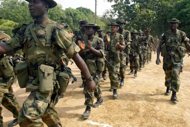 Des militaires en file indienne, certains parmi eux tapent les mains.