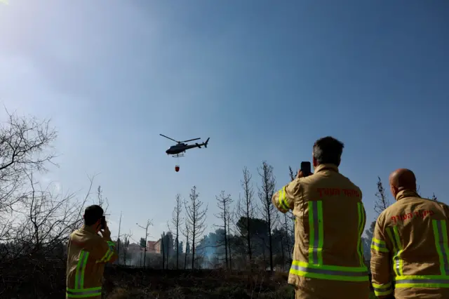 يقف رجل إطفاء بينما تشارك طائرة هليكوبتر في مكافحة الحرائق بالقرب من اللطرون