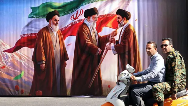 رسم كبير على جدار في شارع طهران فيه علي خامنئي يسلم راية لابنه مجتبى خامنئي وخلف علي خامنئي يقف روح الله الخميني مؤسس الجمهورية الإسلامية في إيران