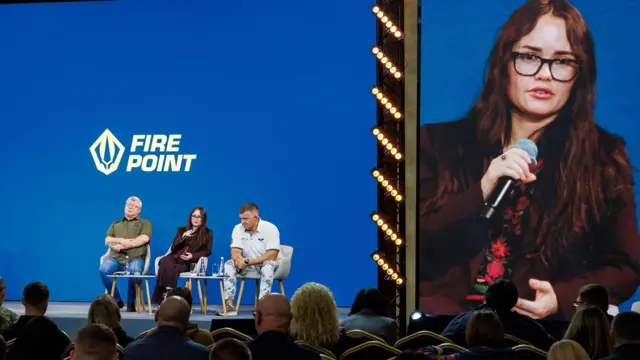 Два мужчины и женщина сидят на сцене.