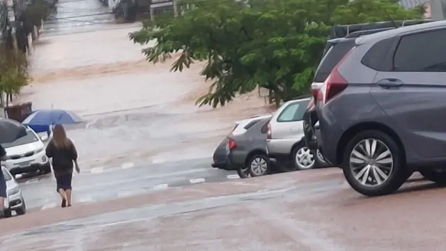 Mulher caminhando na rua com guarda-chuva; na frente dela, está grande volumebet365 north staffordshire reino unidoágua