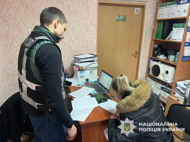 Жінка у відділку поліції підписує документ, сидячи за столом 