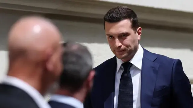 Jordan Bardella, de saco azul oscuro y corbata negra, tiene una expresión seria a la entrada al tribunal de apelaciones.