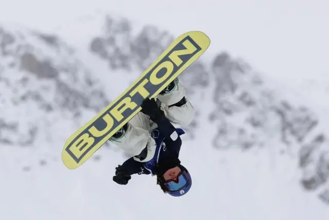 上半身が黒っぽく、下半身が白のウエアを着て、ヘルメットとゴーグルをつけた深田が空中で頭を下にしている。背後には雪をかぶった山並みがぼんやり見える