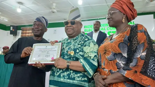 Gomina Ademola Adeleke ree laaarin lasiko to gba iwe ẹri mo yege fun ipo gomina lẹẹkeji. Ọkunrin ati obinrin kan wa ni ẹgbẹ osi ati ọtun rẹ.