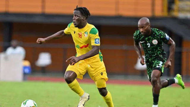 Le Béninois Junior Olaitan (à gauche) court avec le ballon, les bras tendus, et regarde vers la droite lors d'un match de qualification pour la Coupe du monde de football 2026 contre le Nigeria.