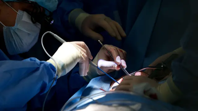 Врачи проводят операцию: на фото видны руки хирурга и его лицо в маске