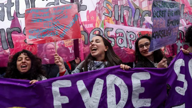 Kadın hakları gruplarının yürüyüşünden bir fotoğraf. Ellerinde pembe ve mor renkli döviz ve pankartlar taşıyorlar.