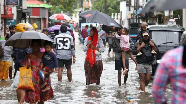 Sri Lankan residents carry their belongings as they evacuate with family members through a submerged road in Wellampitiya, on the outskirts of Colombo, Sri Lanka