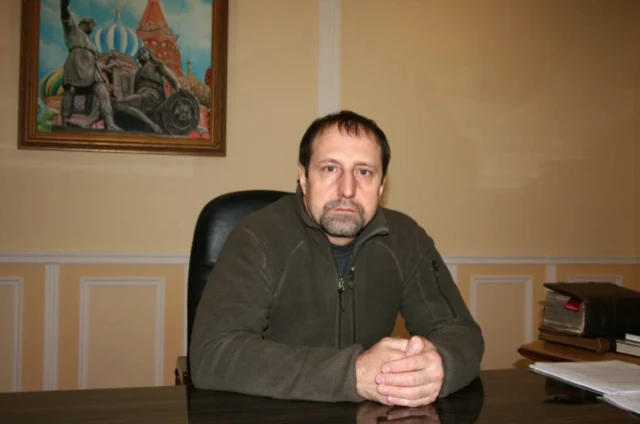 Человек сидит за столом, сложив руки перед собой