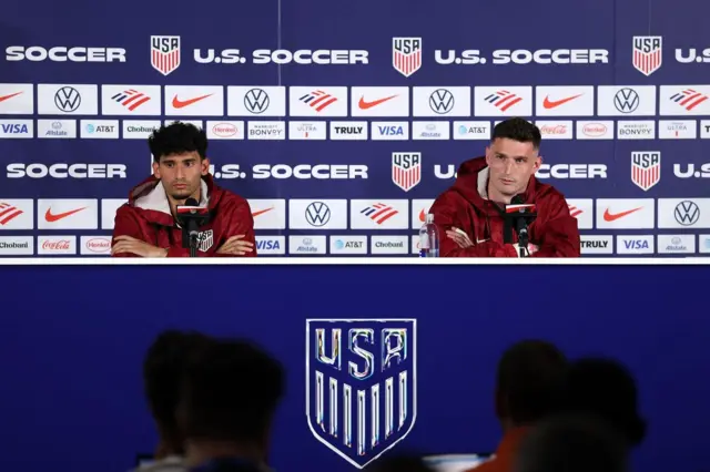 Ricardo Pepi e Matthew Freese, da seleção americana de futebol, durante entrevista coletiva na Califórnia, nos Estados Unidos, em frente aos microfones e tendo atrás uma parede repleta de escudos dos Estados Unidos e logotipos de patrocinadores