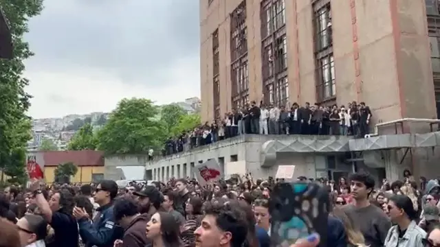 Öğrencilerin bir kısmı avluda, bir kısmıysa alçak katlı bir binanın üstünde protesto ediyor.