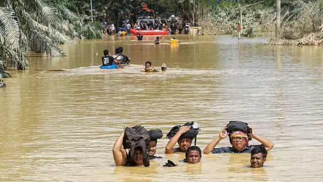 Sejumlah warga di Aceh menerobos genangan air setinggi leher pada 30 November 2025.