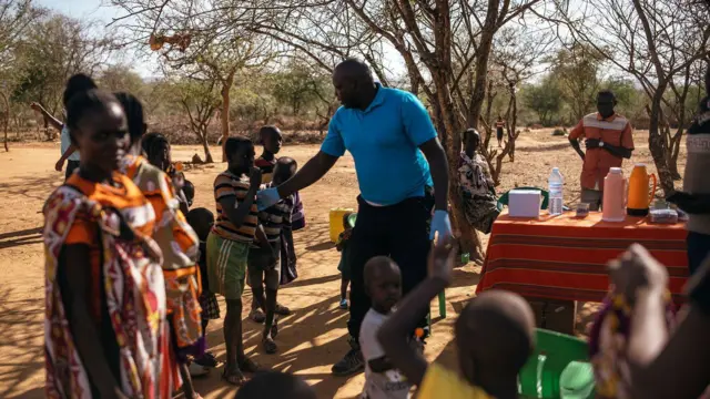 Andrew Ochieng examina a un grupo de personas en su clínica improvisada de leishmaniasis visceral, a la sombra de un árbol en Akorikeya.