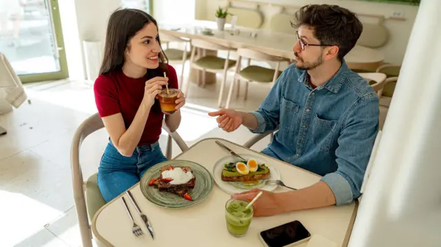 Casal millennial comendo torradas com abacate em uma cafeteria moderna