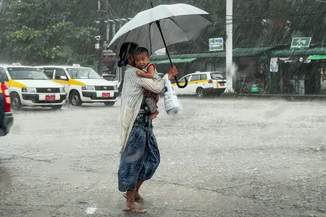  မိုးကြီးတဲ့နေ့မှာ ကလေးချီရင်း ထီးတစ်ချောင်းနဲ့ လမ်းဖြတ်ကူးနေတဲ့ အမျိုးသမီး 
