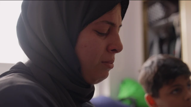 A woman has closed her eyes and looks on the verge of tears. A child can be seen in the background.