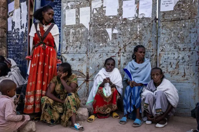 ኣብ ትጽቢት ዘለዋ ዝመስላ ኣንስቲ ብሰንፈላል ኣብ ኣፍደገ ሓደ ዝተዓጽወ ዓቢ ማዕጾ ኮፍ ኢለን ከለዋ