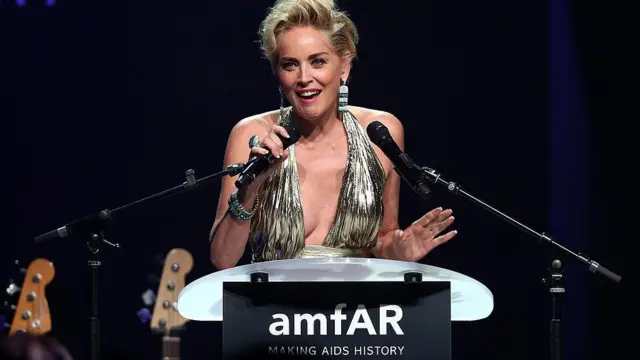 Sharon Stone com vestido prateado falando no microfone