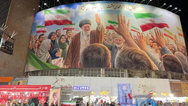 Большая фреска с изображением покойного аятоллы висит над оживленной торговой улицей.