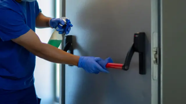 Homem de máscara limpando porta de emergência