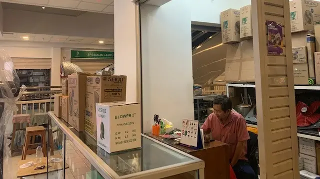 Pria duduk di belakang meja kayu yang dipenuhi kardus-kardus kipas angin