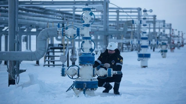 مردی در حال کار روی بخشی از تاسیسات گاز و نفت، فضای کار از برف سفیدپوش شده است