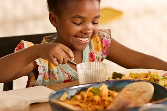 Fille souriante, mangeant son dîner à table