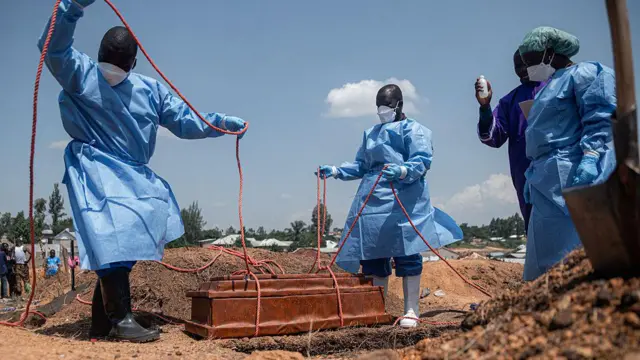 Abantu bane bambaye impuzu zidasanzwe zibakingira indwara bariko barururutsa isandugu irimwo ikiziga mu mva bakoresheje imigozi.