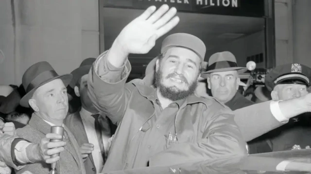 A black and white picture of former Cuban leader Fidel Castro waving to a camera and smiling.