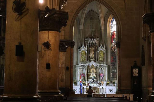 Parte interna da igreja, onde uma mulher ergue os braços enquanto reza 