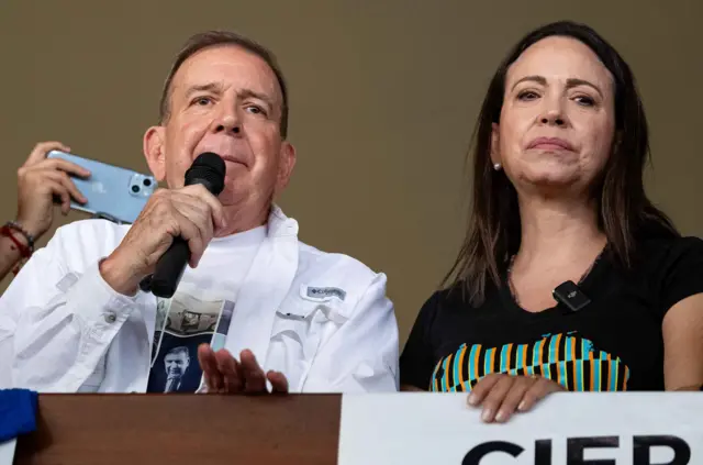 Edmundo González Urrutia e María Corina Machado; ele veste camisa branca e segura microfone; ela veste camiseta preta