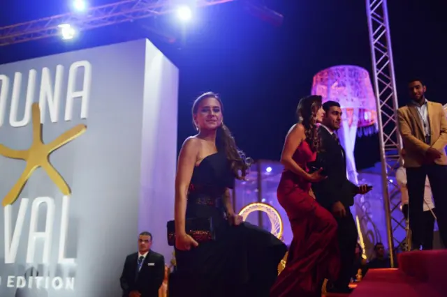 الممثلة المصرية نيللي كريم تقف على السجادة الحمراء مرتدية فستاناً أسود اللون وتلتفت نحو عدسات المصورين خلال حفل ختام مهرجان الجونة السينمائي، مع خلفية تحمل شعار المهرجان وأضواء الكاميرات عام 2018