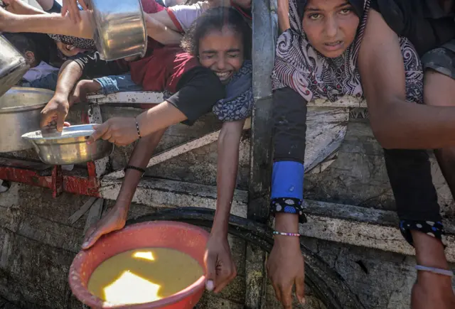 Interno raseljeni Palestinci i mala deca, drže lonce dok dobijaju hranu iz dobrotvorne kuhinje u gradu Gazi 4. avgusta 2025.