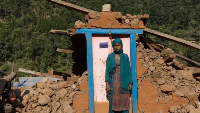 जाजरकोट भूकम्पबाट भत्किएको घरअगाडि उभिएकी नेपाली महिला