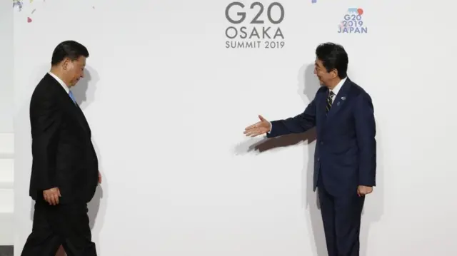 中国国家主席习近平低头走向面带微笑、伸出手的日本首相安倍晋三。