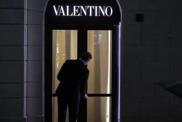 「VALENTINO」と白い文字が黒い扉の上に浮かび上がる、夜の写真。黒いスーツ姿の男性が扉に鍵をかけているように見える