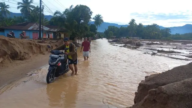 Seorang pria mendorong motor di tengah banjir di Tapanuli Tengah.