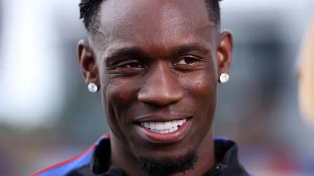 Balogun con dos diamantes en cada oreja sonrie a la cámara.