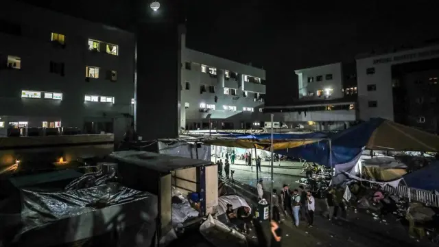 Tendas na escuridão com edifícios ao fundo com luzes nas janelas