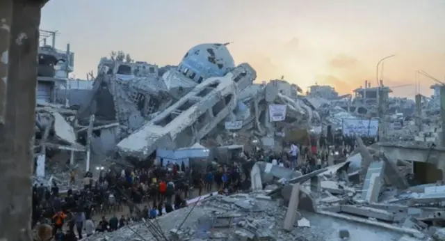 Руїни в Газі - гори бетону, цегли, арматури. Серед них стоїть натовп. 