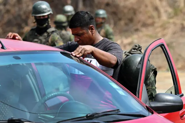 Soldados equatorianos armados e mascarados recebem um homem e seu carro