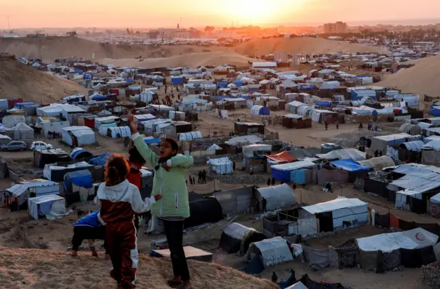 Dos menores desplazados palestinos conversan en un asentamiento de refugiados en Jan Younis. Detrás, el sol se pone en el horizonte. 